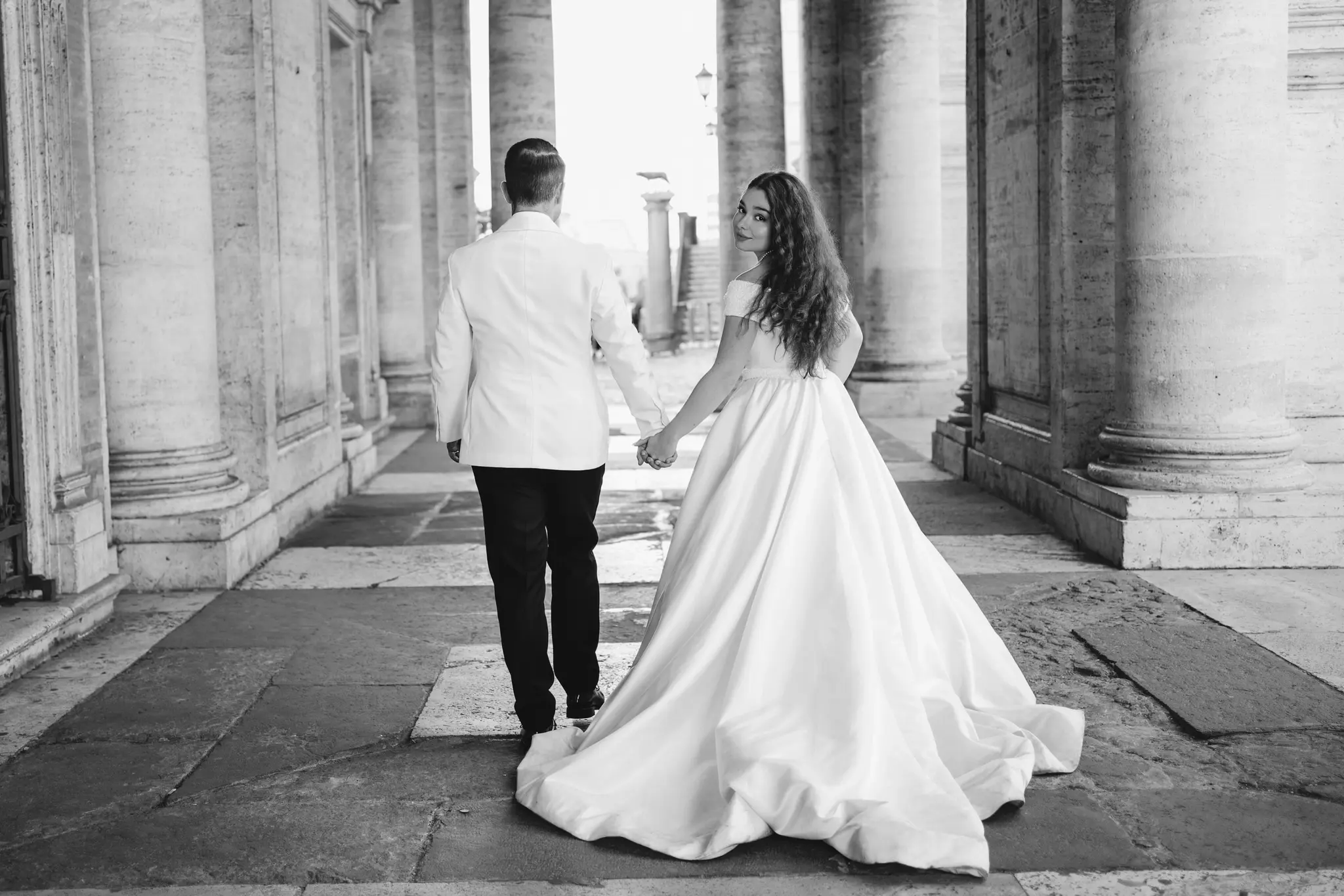 Newlyweds strolling hand in hand beneath ancient Roman columns, tips on how to get married in Italy as an American easily.