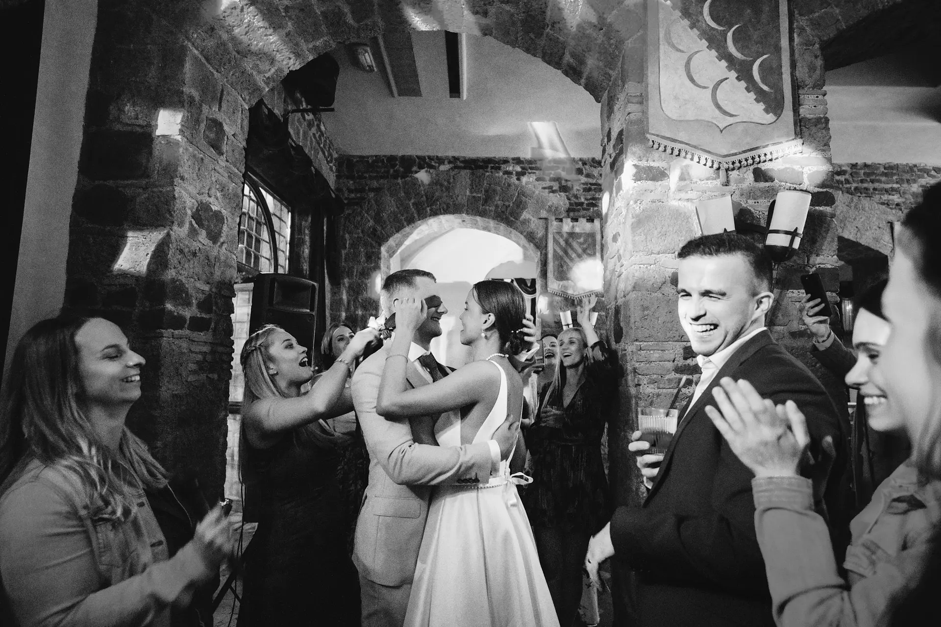 B&w, newly married hug. First dance with great cheers by old and stone construction.