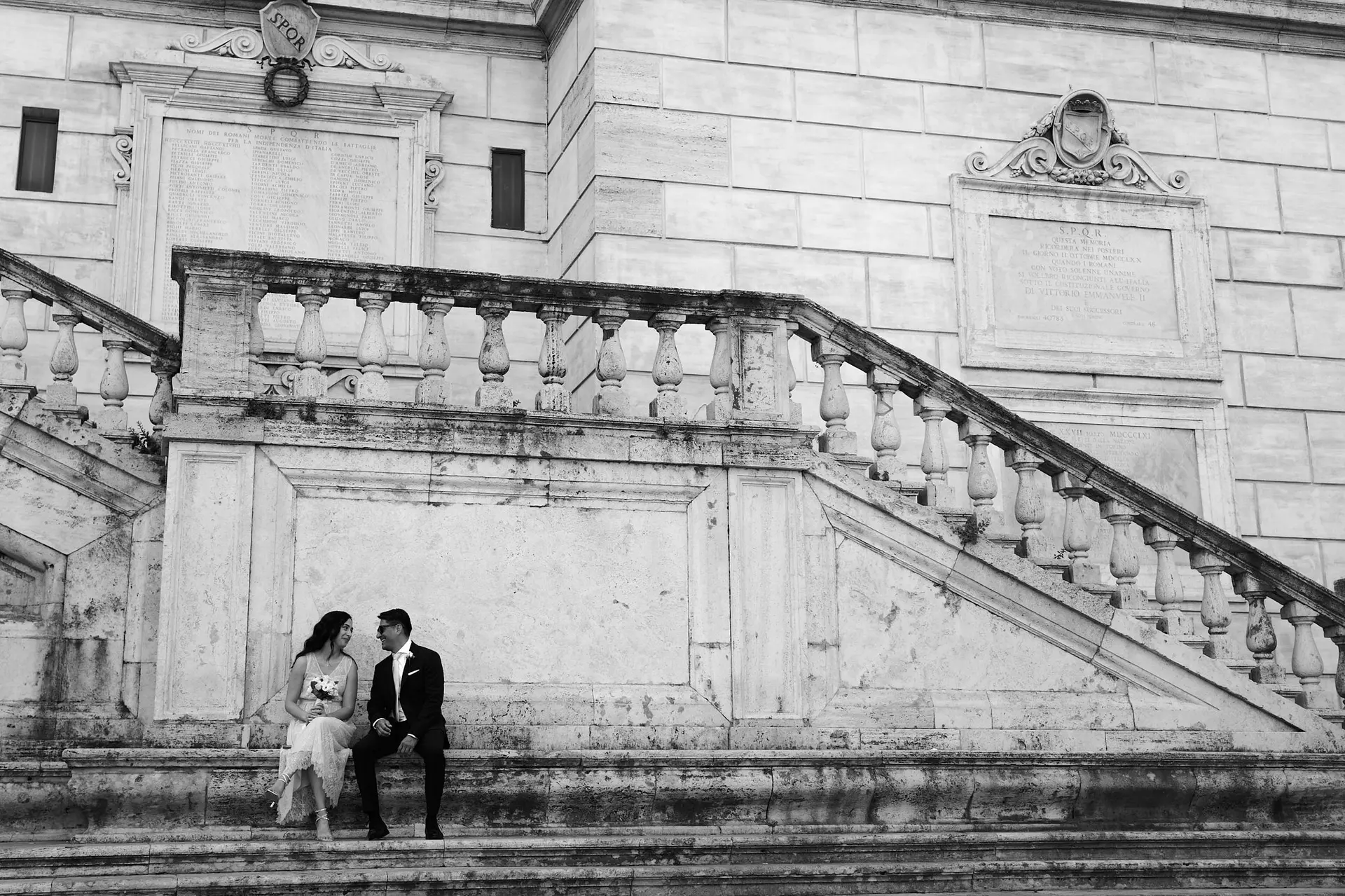 Bride and groom practice posing on stone steps of grand building during their wedding rehearsal photo session.