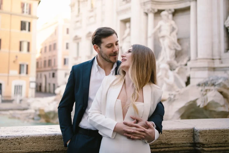 Happy couple in stylish outfits embrace in front of the Trevi Fountain.