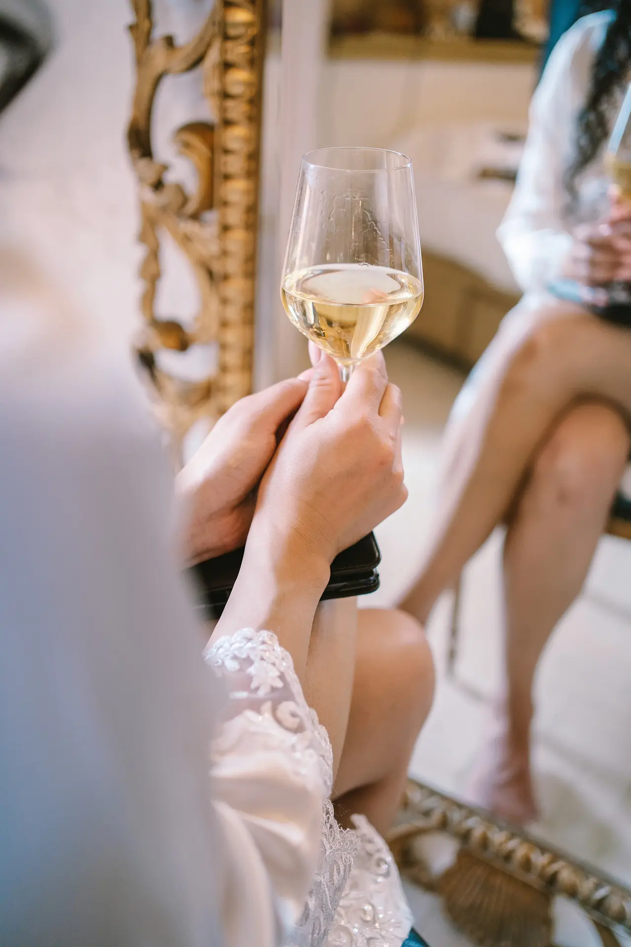 Close up of a woman in a white lace robe holding a glass of white wine.