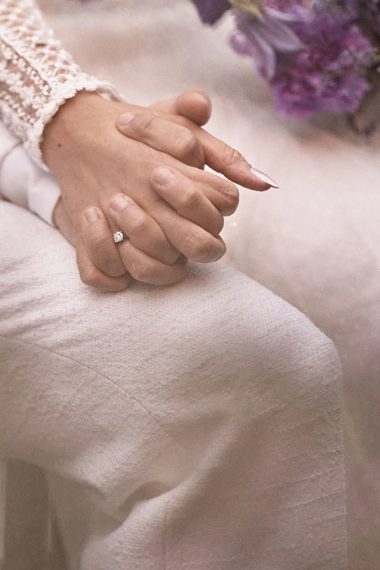 Close up of a couple holding hands, showing a diamond engagement ring.