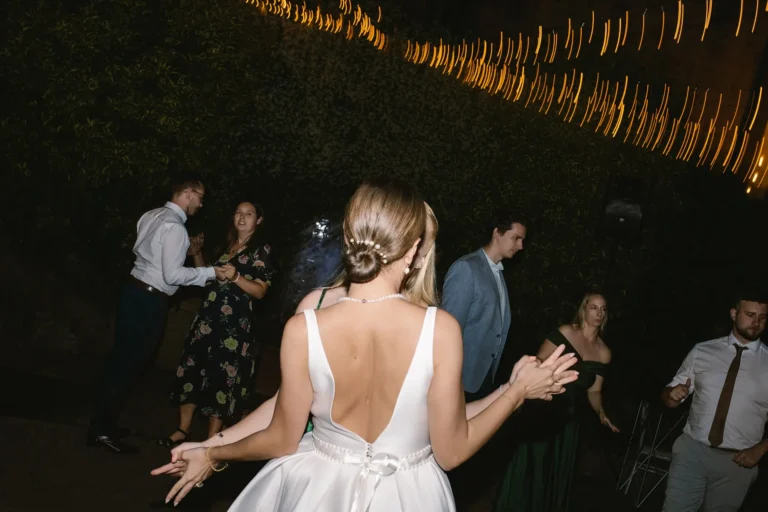 Bride with pearl hair bun dances to lively Italian wedding music at night reception under string lights.