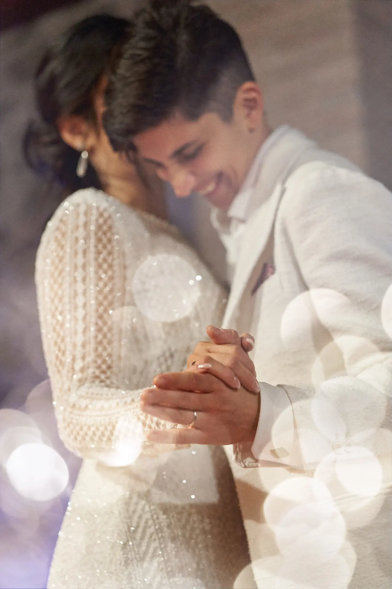 Soft focus close-up of a wedding couple in white tenderly dancing, hands clasped, joyful smile.