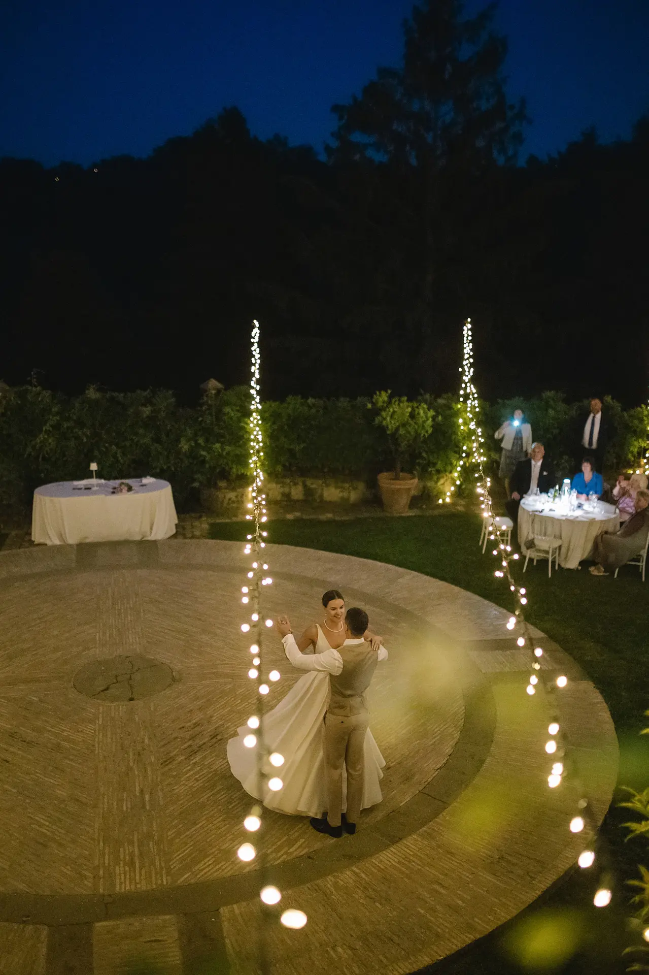 Couple's first dance on patio with string lights, perfect setting for Italian wedding music.