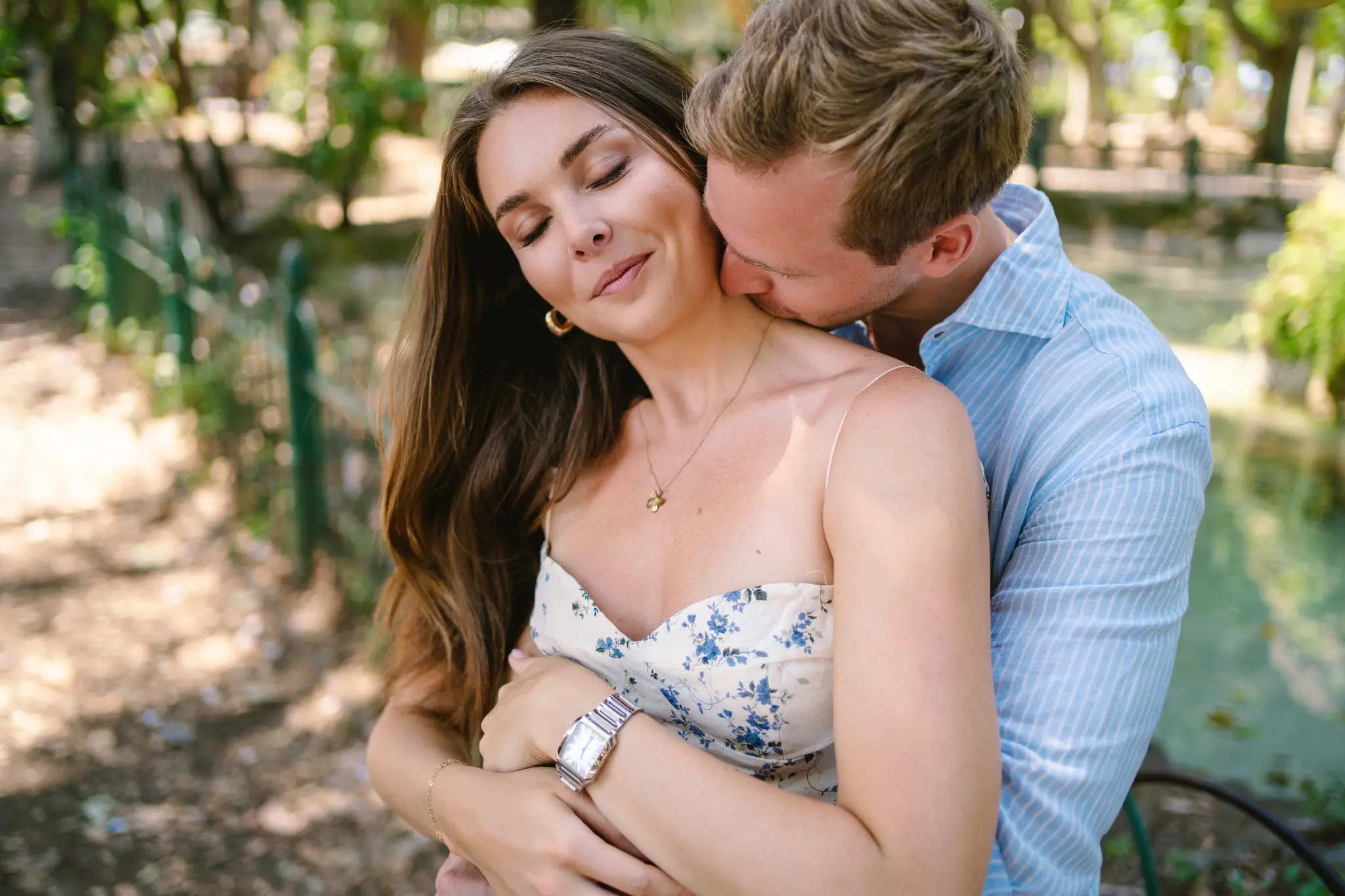 A man tenderly kisses a woman's neck in Villa Borghese after getting engaged.
