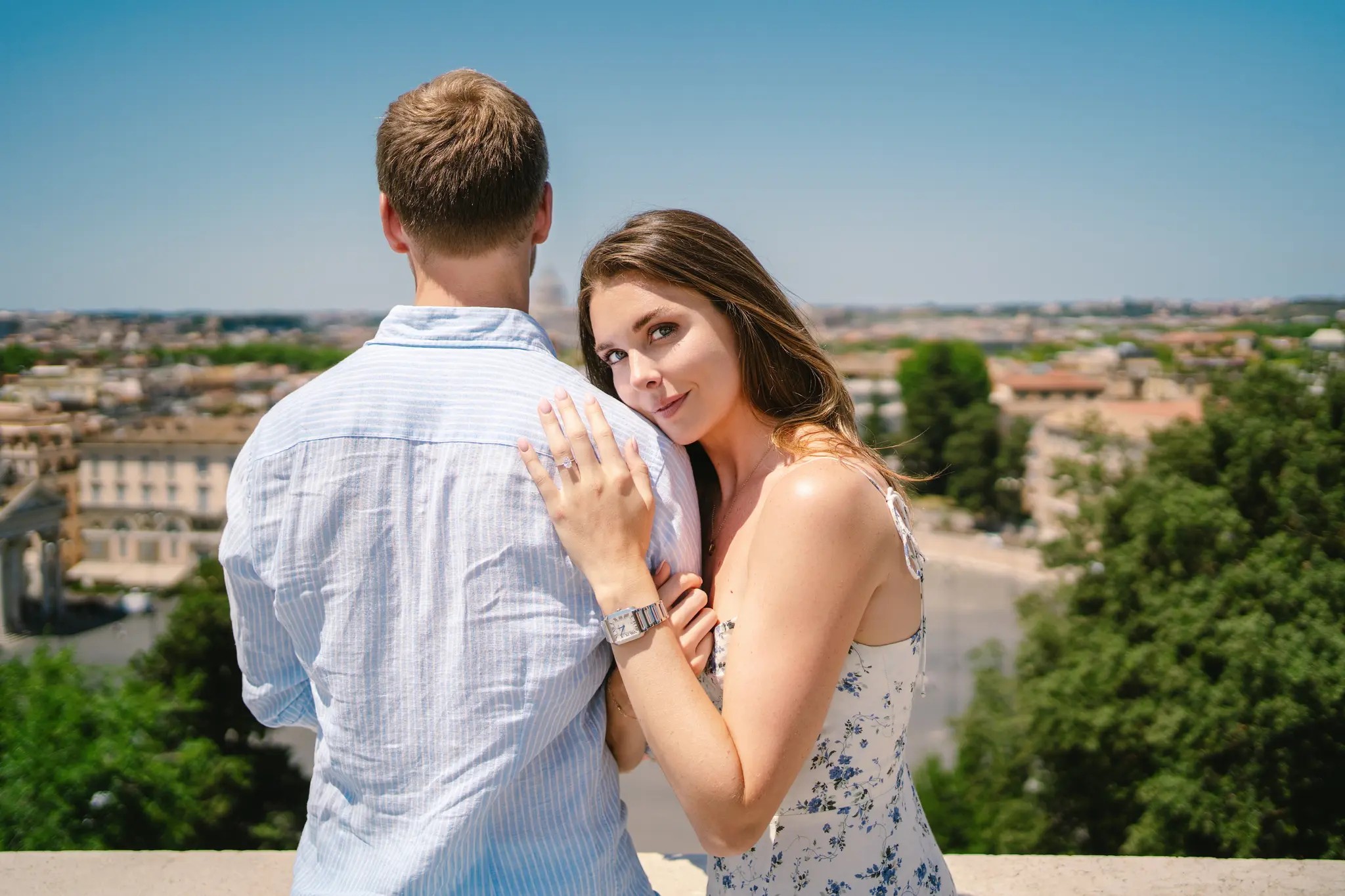 Woman leans on man's shoulder, viewing a cityscape from Villa Borghese.