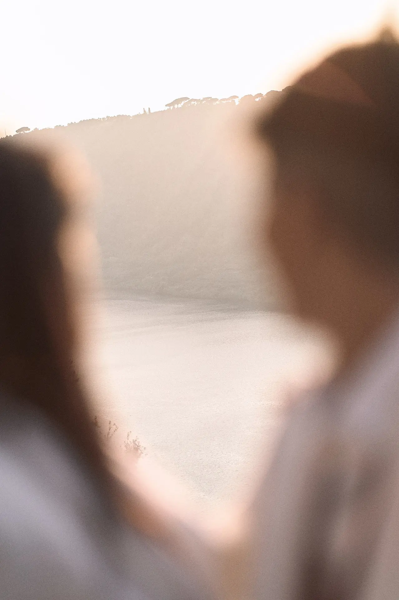 Two women, out of focus, gaze at a hazy, sunlit landscape.