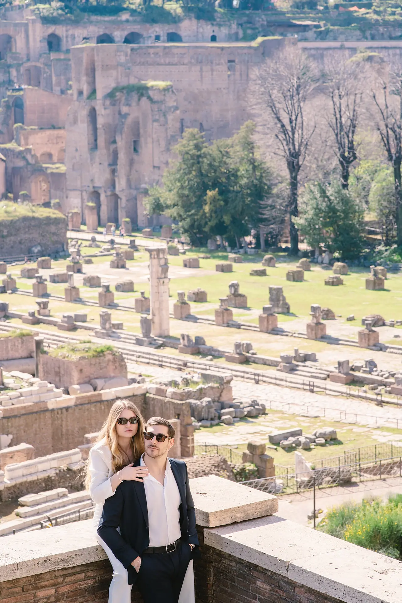 A stylish couple in sunglasses poses overlooking the Roman Forum, an iconic engagement photo location.
