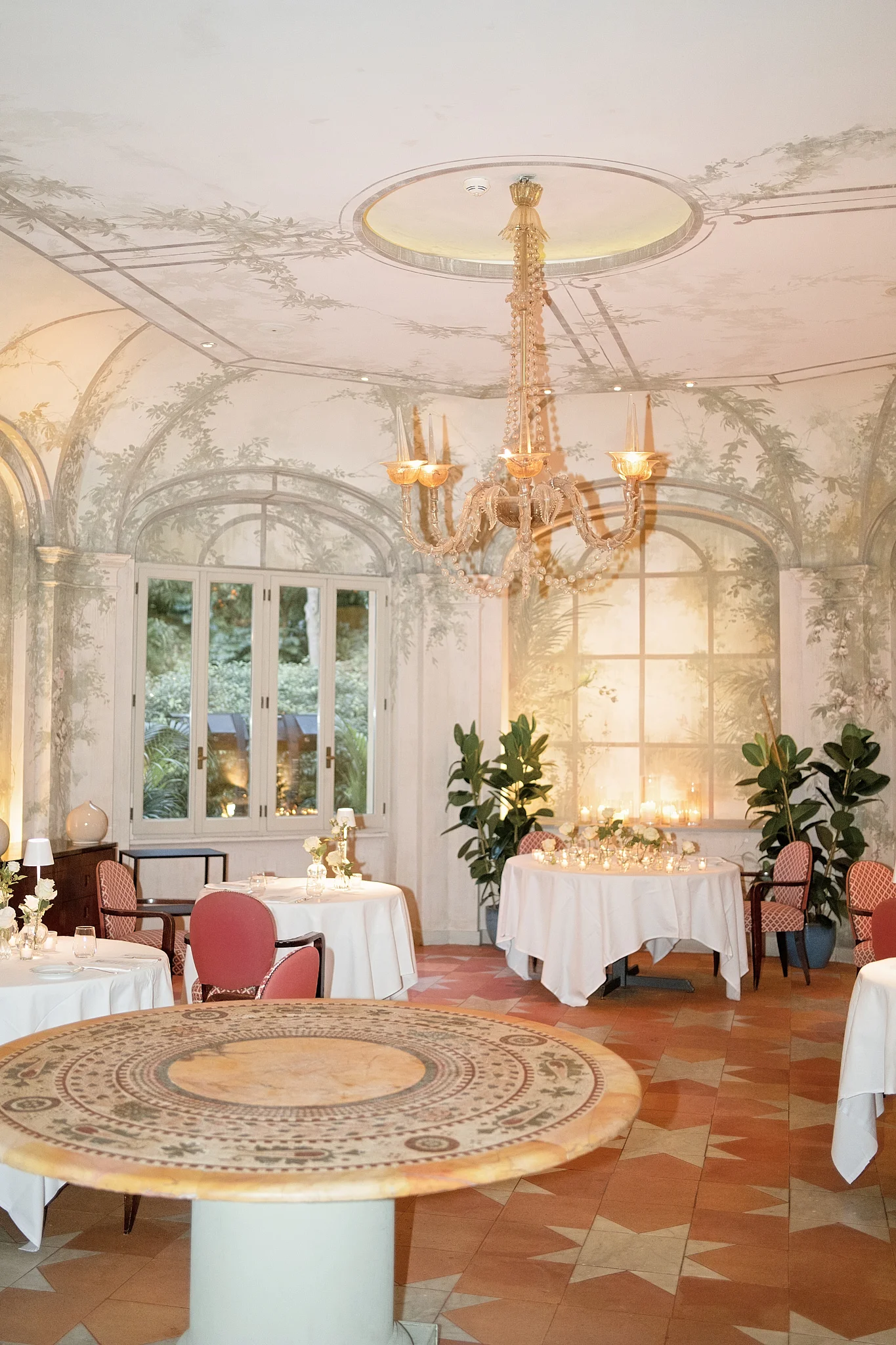 Reception room with painted murals, a chandelier, star-patterned tile floor, and dining tables.