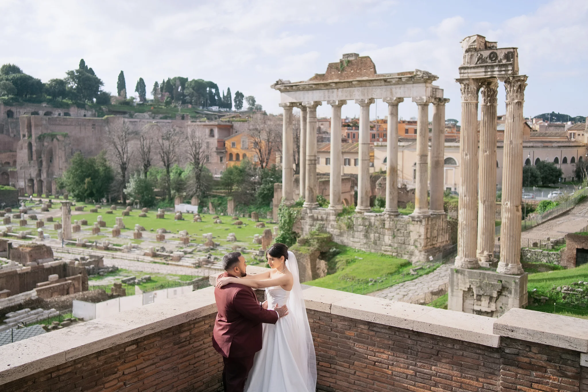 A couple embraces on a balcony, a perfect example of how to elope in Italy with the Roman Forum behind.