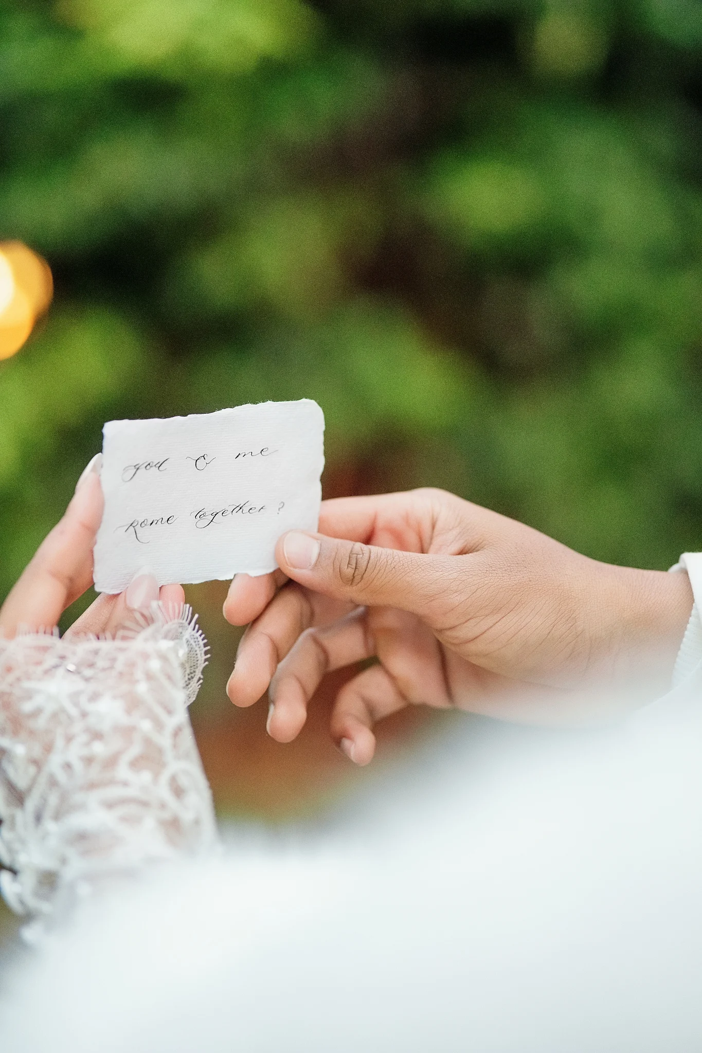 A bride and groom's hands hold a romantic, handwritten calligraphy note with torn edges.