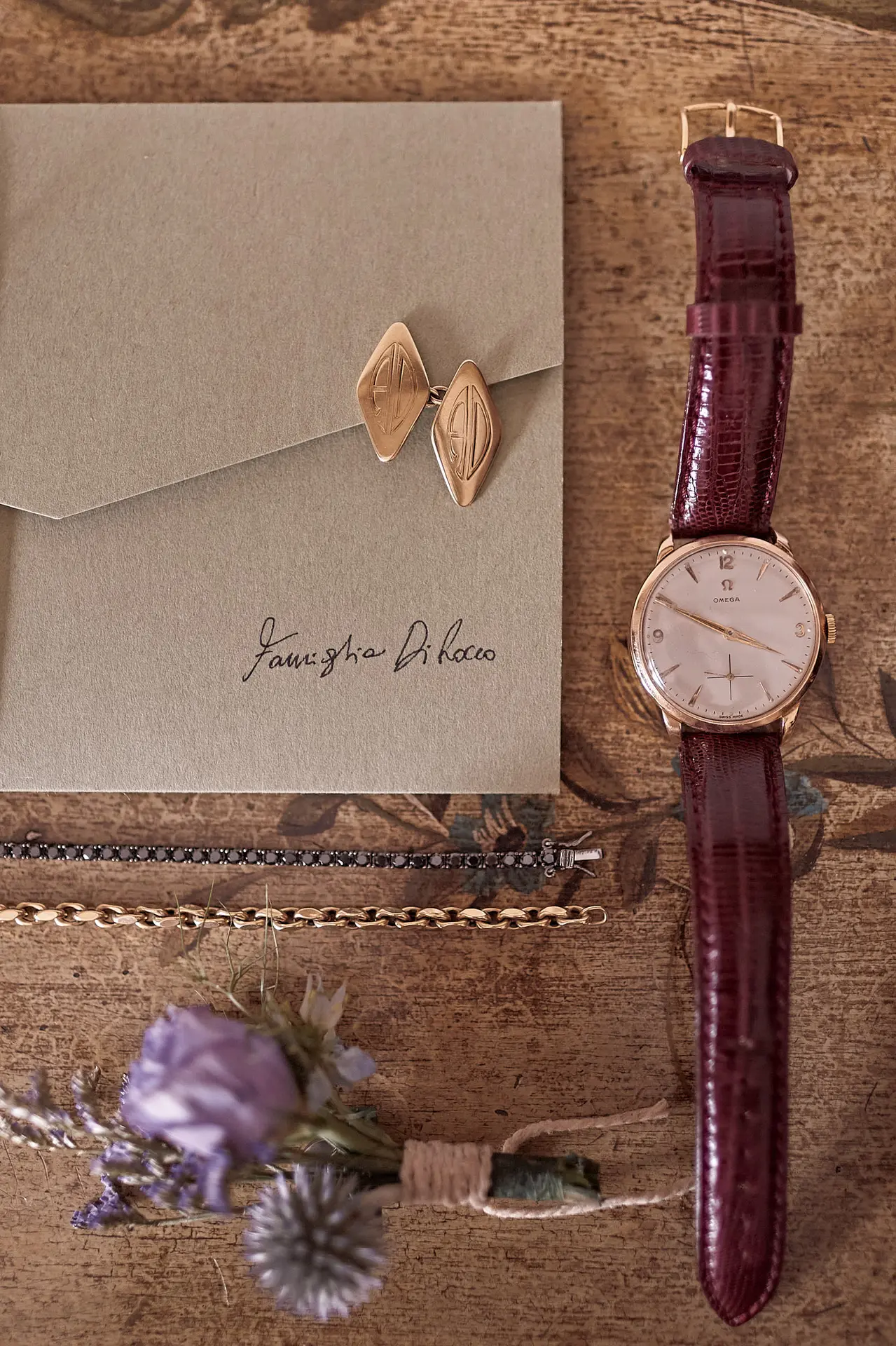 Groom's wedding accessories: a vintage Omega watch, cufflinks, and a boutonniere on a wood surface.