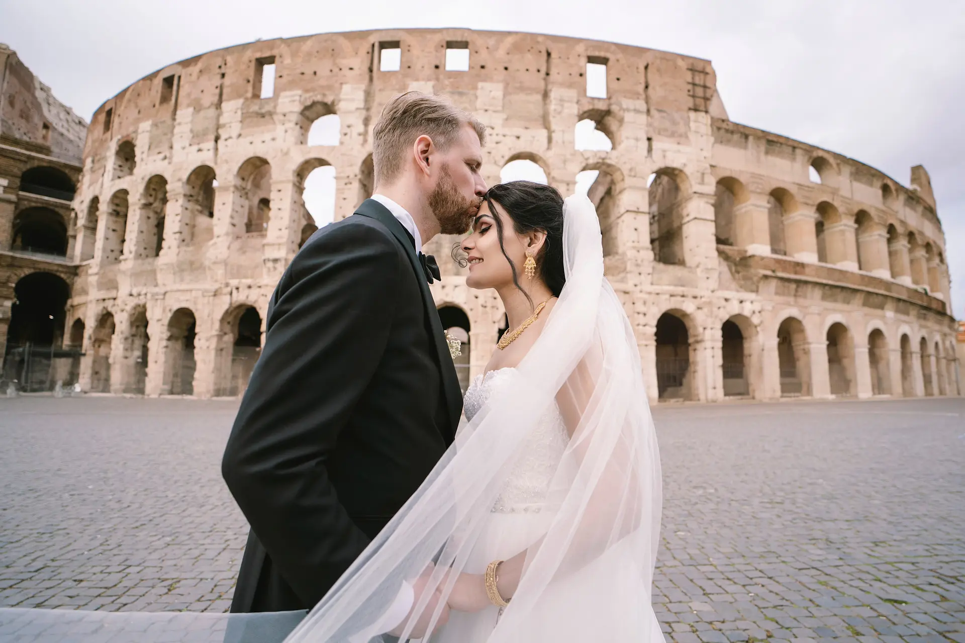 A groom kisses his bride's forehead before the Colosseum, a key part of how to plan a destination wedding in Italy.