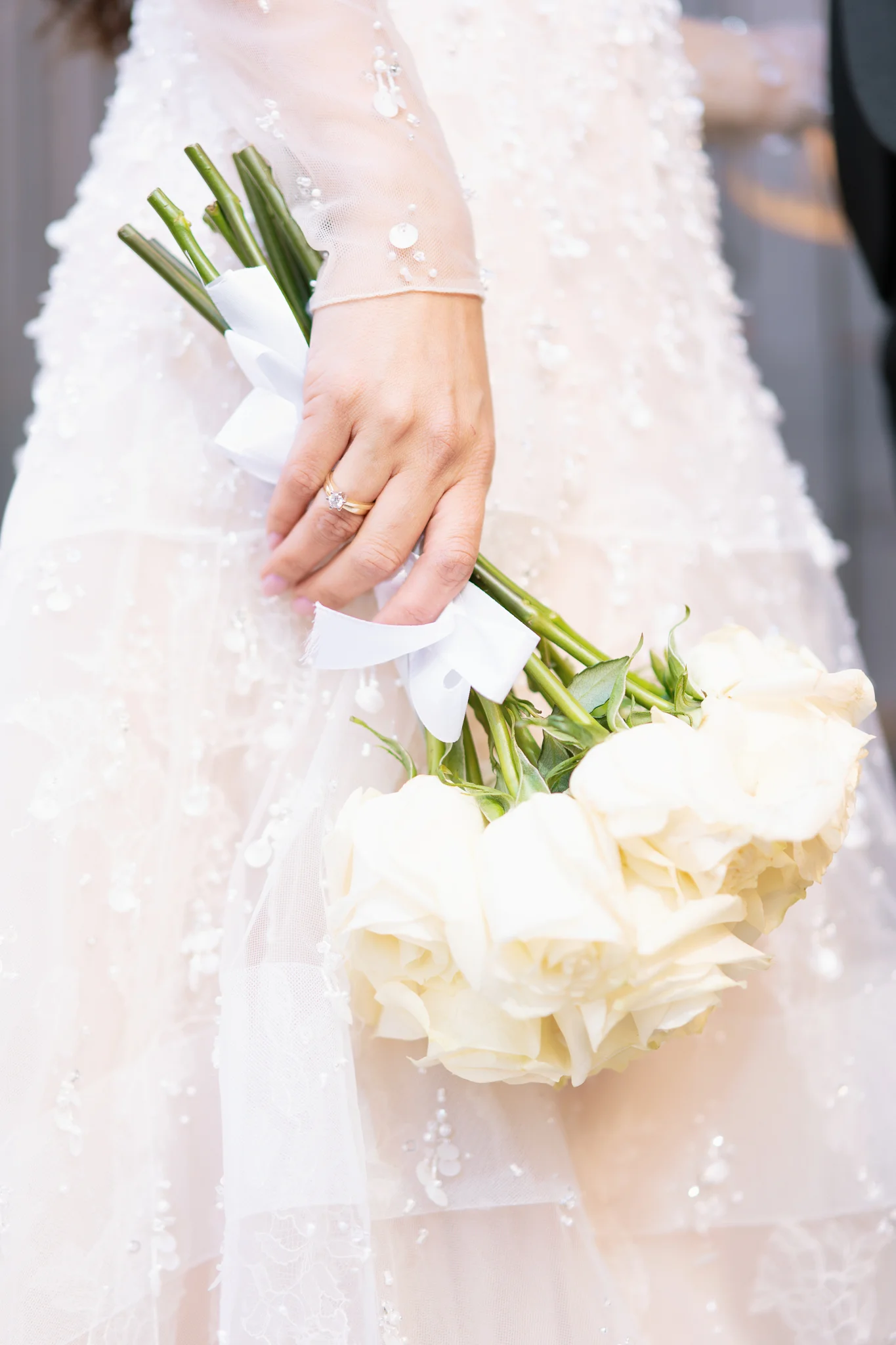 Close-up on a bride's hand with her wedding ring, gently holding a bouquet of cream-colored roses.