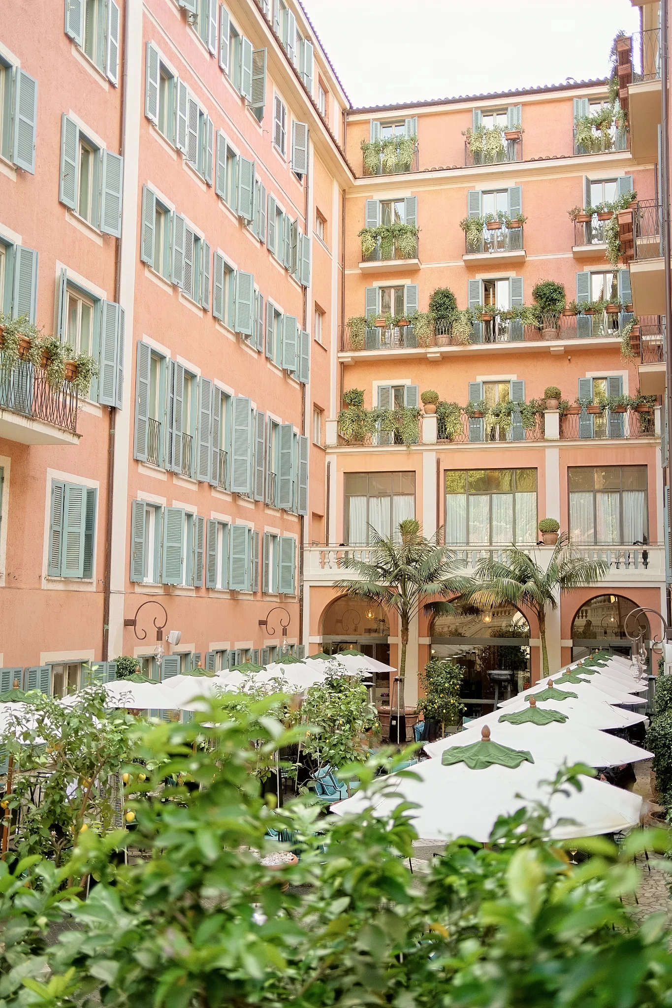 A picturesque Italian hotel courtyard with pink walls, green shutters, and white parasols for a reception.