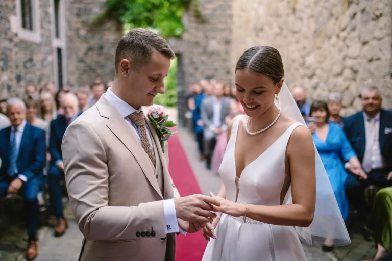 A groom puts a wedding ring on the smiling bride's finger during an outdoor ceremony.