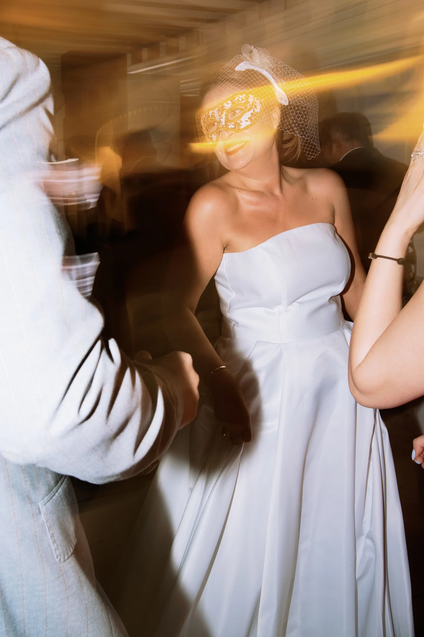 An artistic, motion-blur photo of a happy bride in a mask dancing at her wedding reception.