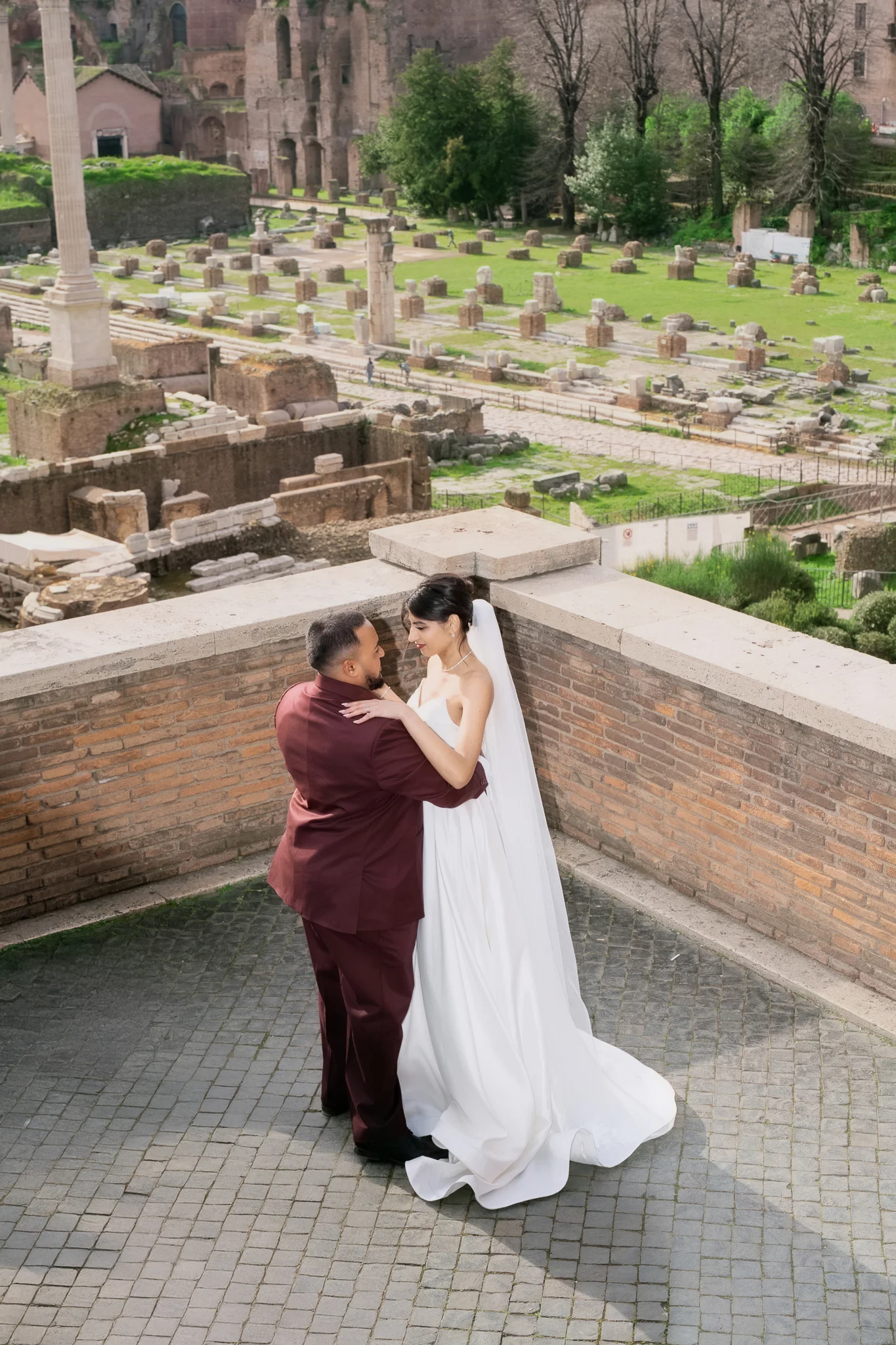 A bride and groom embrace on a terrace overlooking the ancient ruins of the Roman Forum.