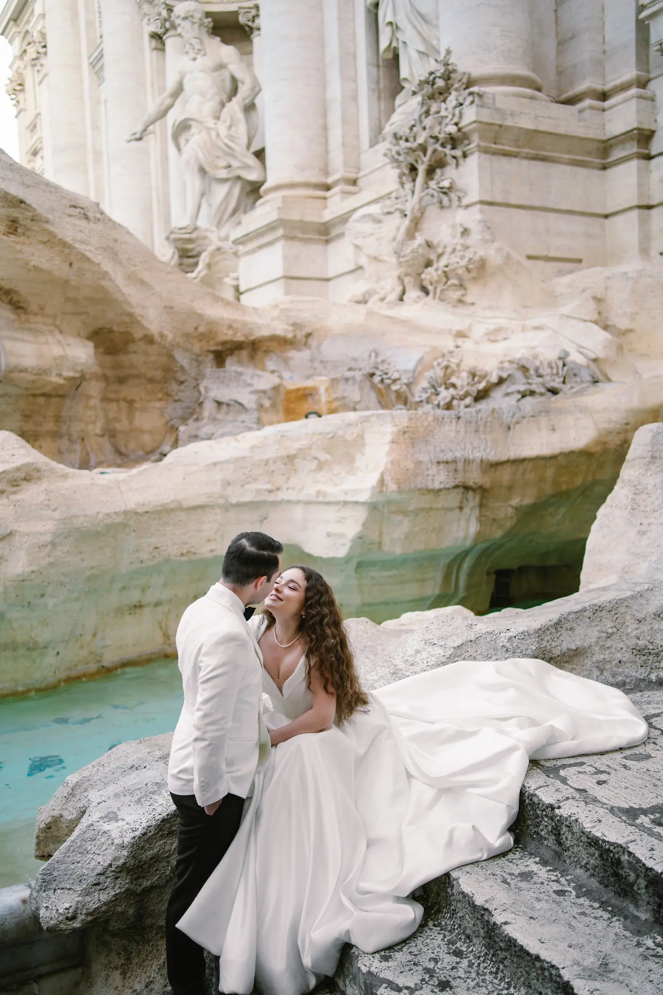 A newlywed couple shares an intimate and romantic moment by the iconic Trevi Fountain in Rome.