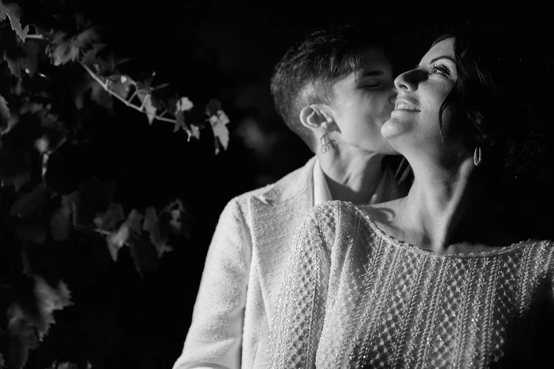An intimate nighttime black-and-white photo of a couple sharing a tender embrace under soft lighting.