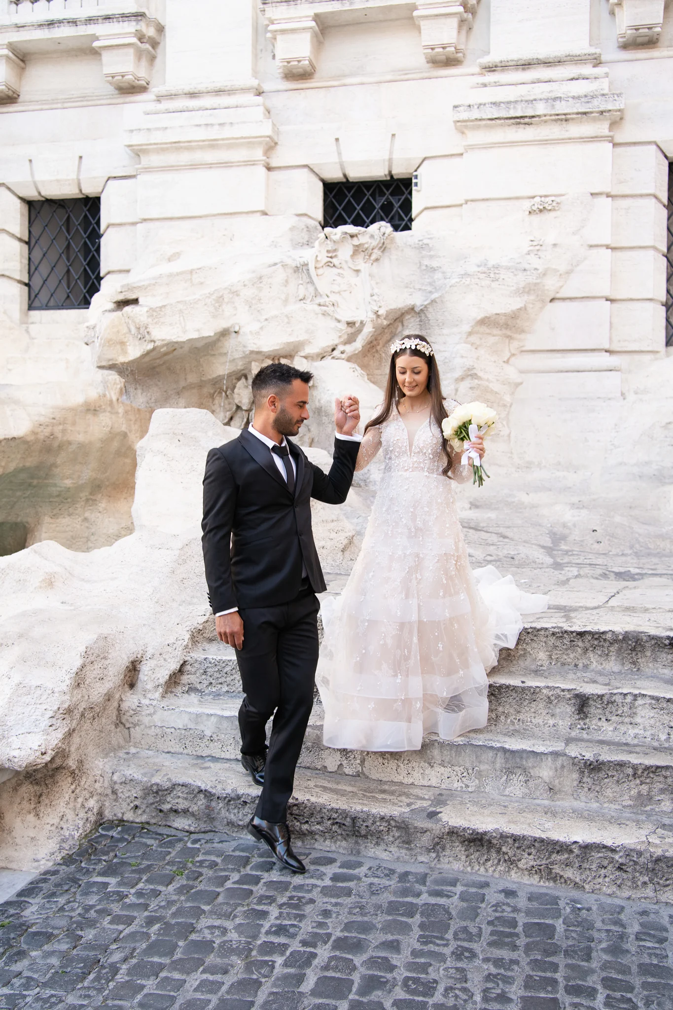 A groom helps his bride down ancient stone steps in Rome, a moment captured by a professional photographer for Italy weddings.
