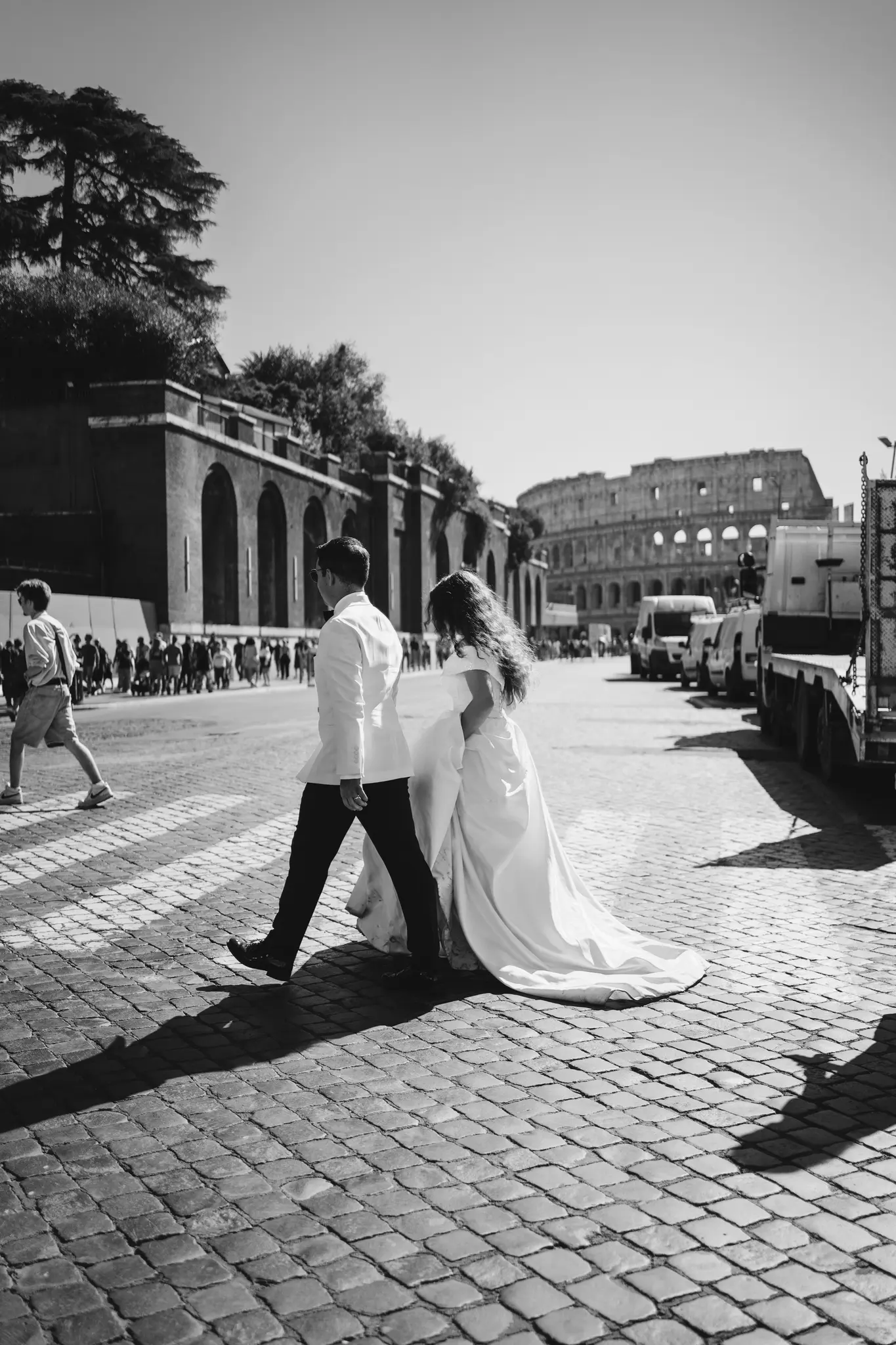 A professional photographer for Italy weddings shoots a candid B&W of a couple walking on cobblestones with the Colosseum in the background.