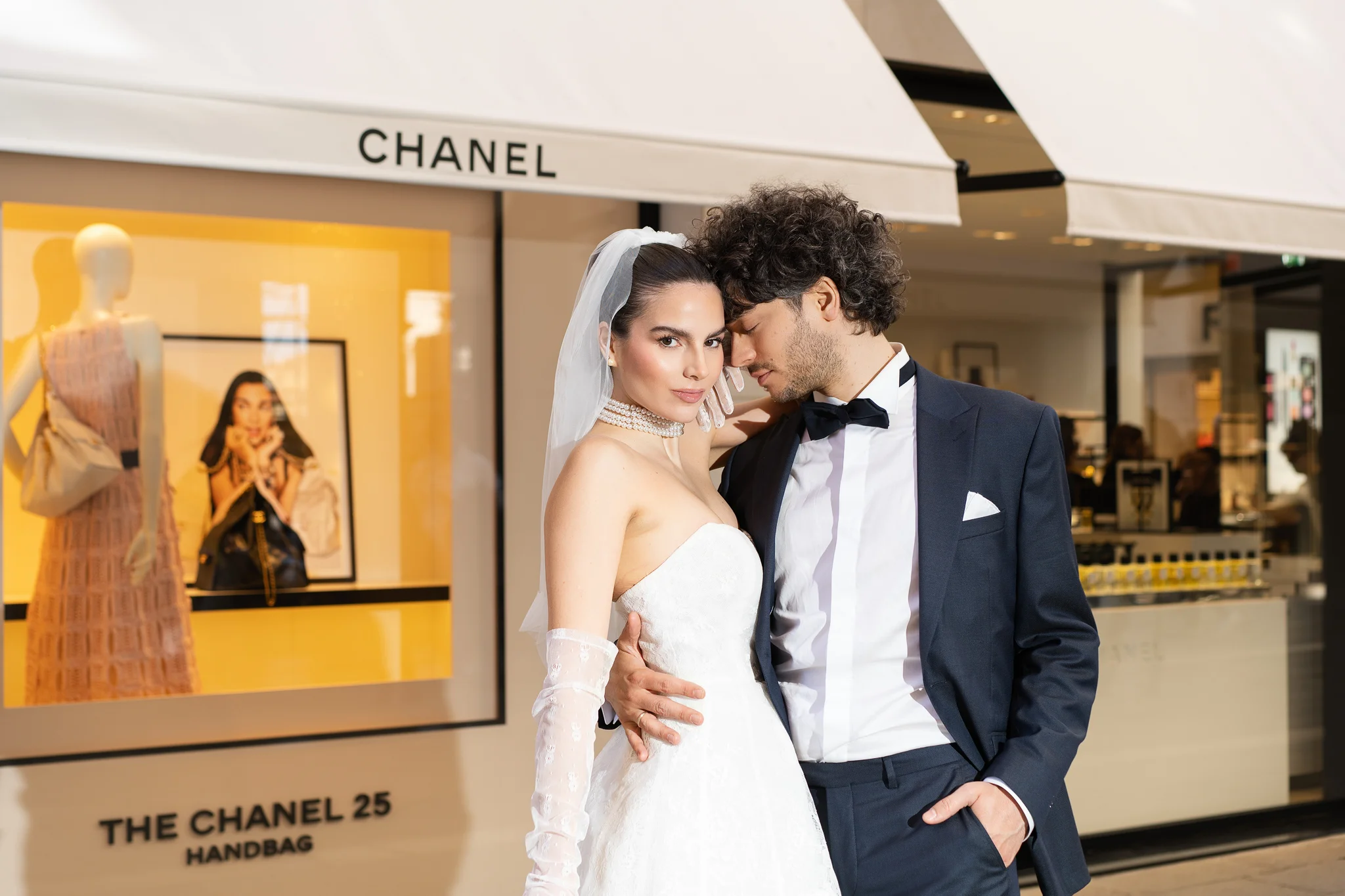 A glamorous bride and groom share an intimate moment while posing for photos in front of a Chanel boutique.