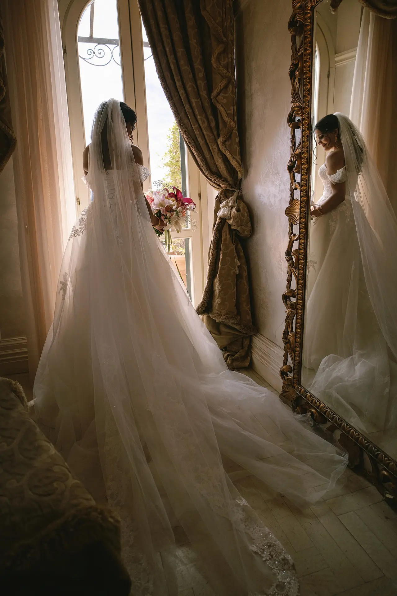 A bride in her gown looks in a mirror. Such artful shots affect the wedding photographer cost in Italy.