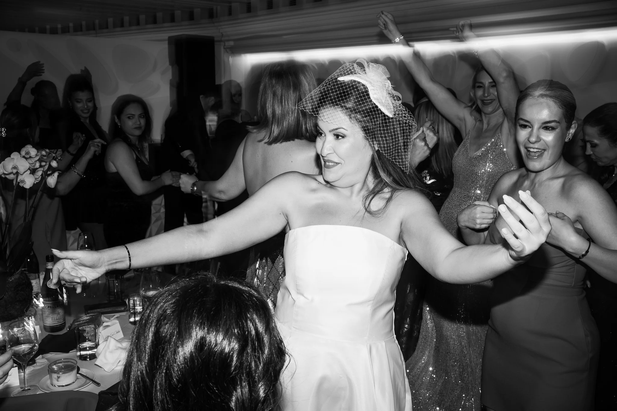 B&W: A joyful bride wearing a birdcage veil dances happily at her wedding reception party.