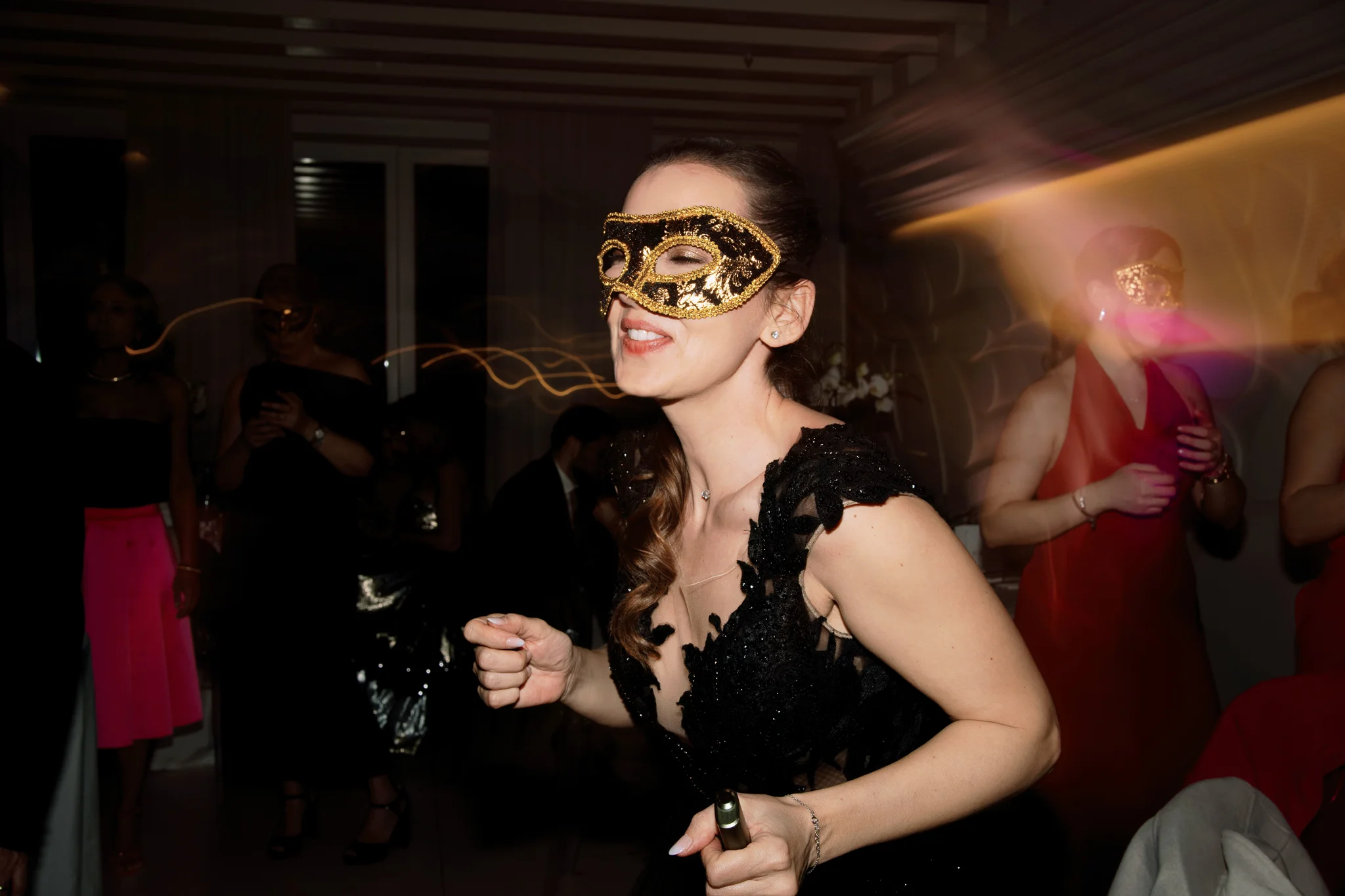 A guest in a glittery gold mask smiles and dances during a lively wedding reception in Italy.