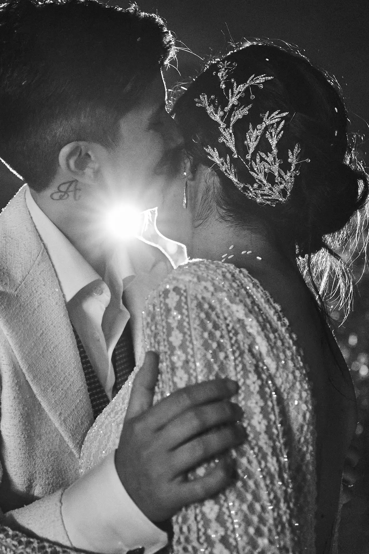 A romantic, backlit black and white photo shows two brides sharing an intimate kiss.
