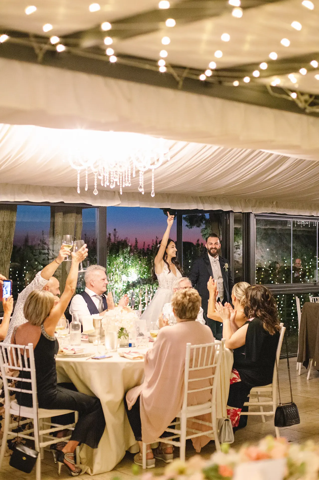 A wedding second shooter in Italy captures the moment a bride and groom are toasted by guests at dinner.