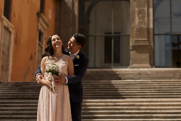 A happy couple enjoys their affordable destination wedding in Italy on sunlit stone steps.