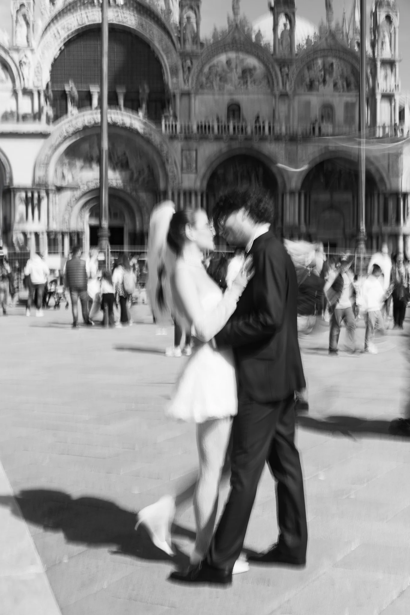 Motion-blur, black and white photo of a couple kissing in St. Mark's Square, Venice.