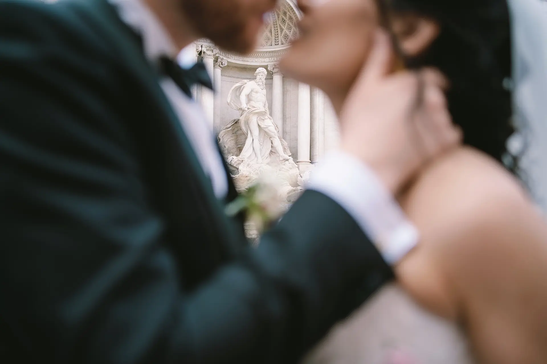 A romantic kiss is beautifully framed between the bride and groom, with the Trevi Fountain in focus.