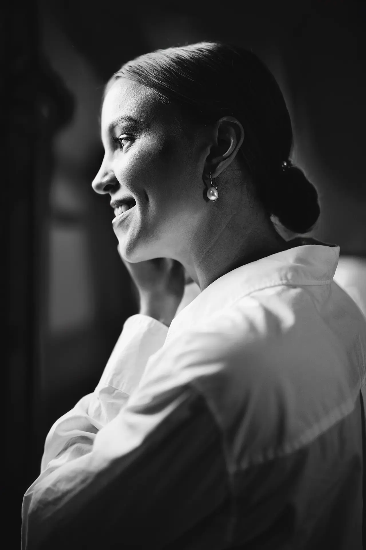 A striking black and white profile of a woman smiling, her face gently lit, wearing a pearl earring.
