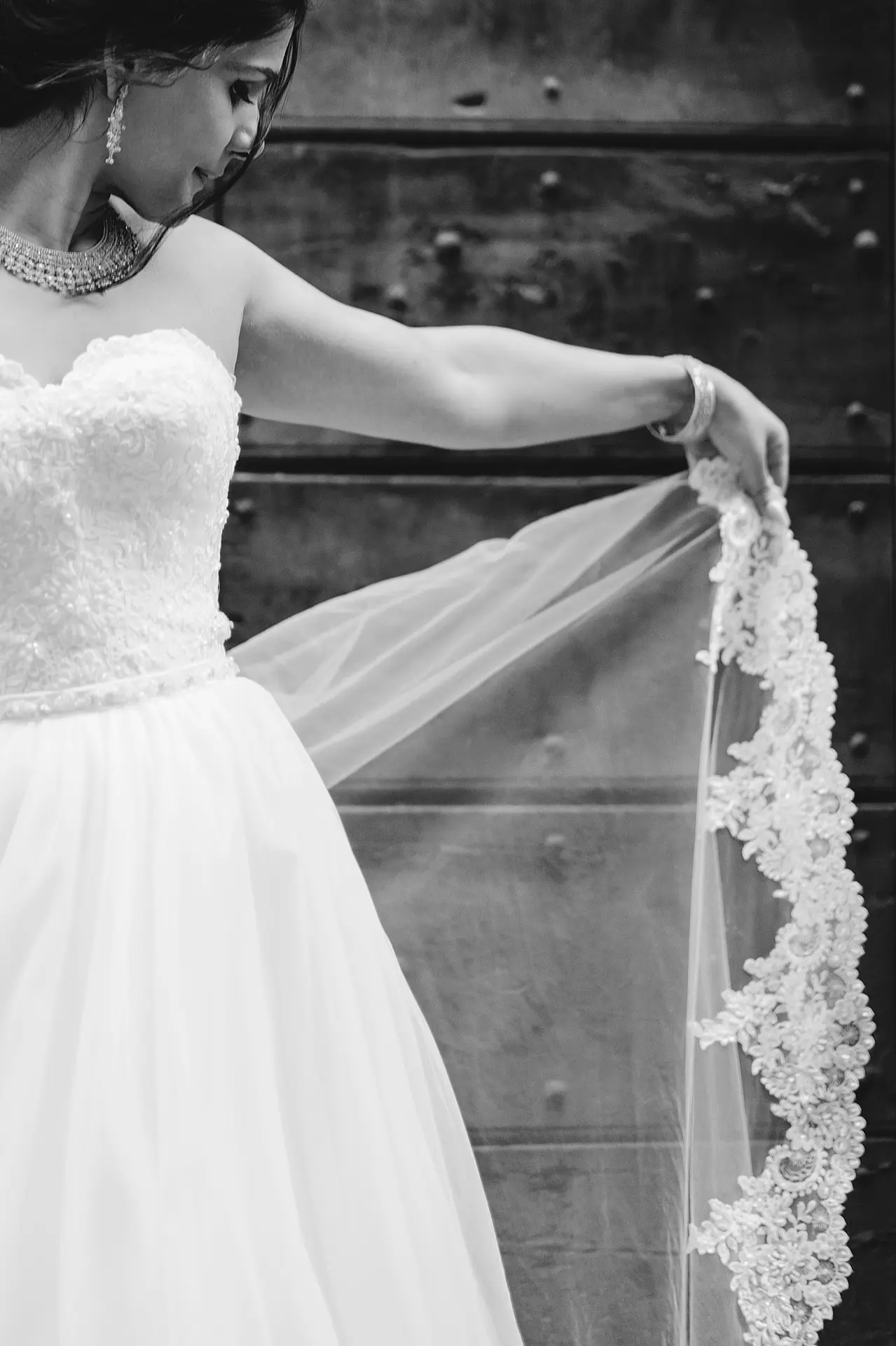 A detailed black and white shot focuses on a bride’s hand as she delicately holds her intricate lace veil.