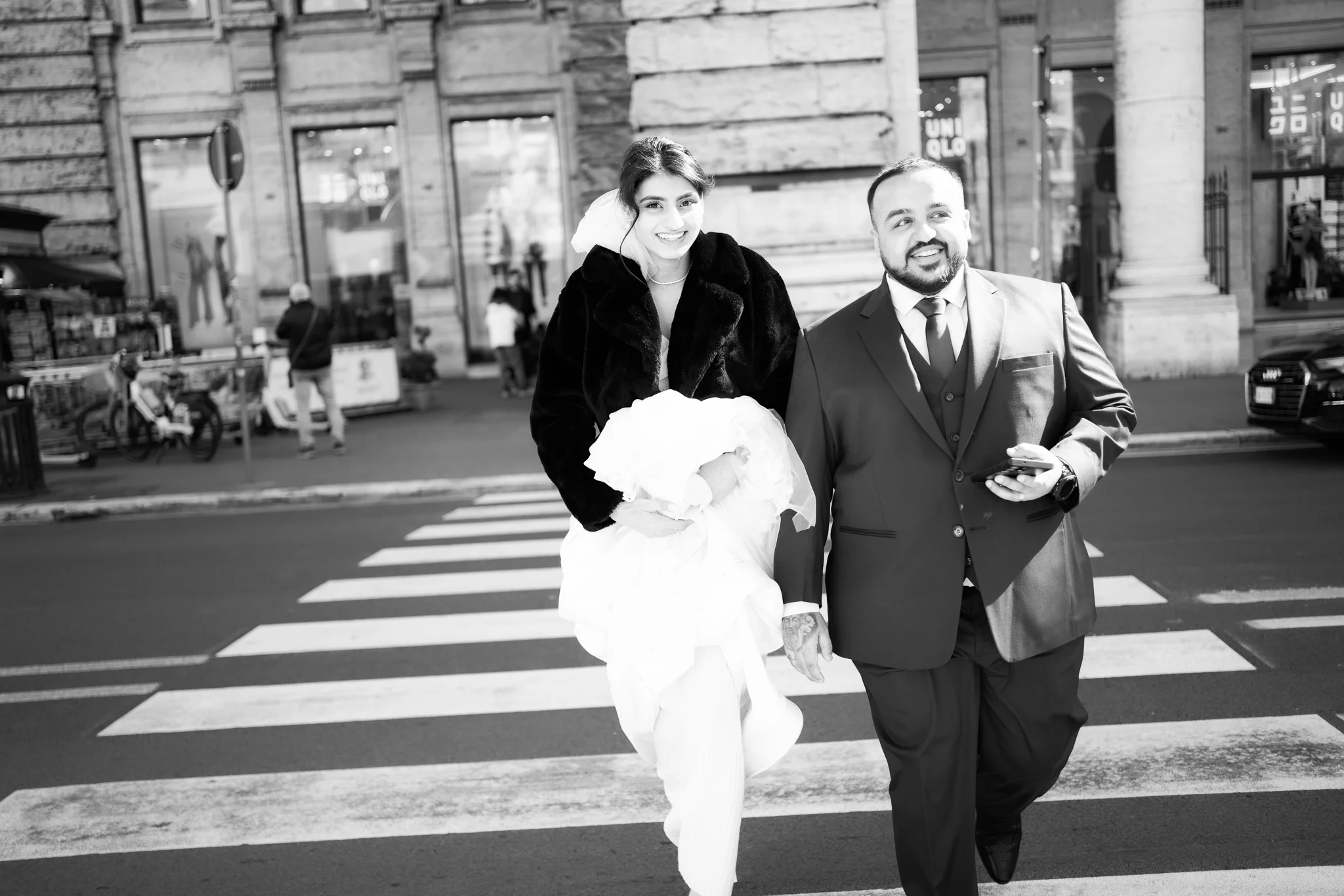 A smiling bride and groom cross a street in the city. A great urban shot by a wedding photographer in Rome.