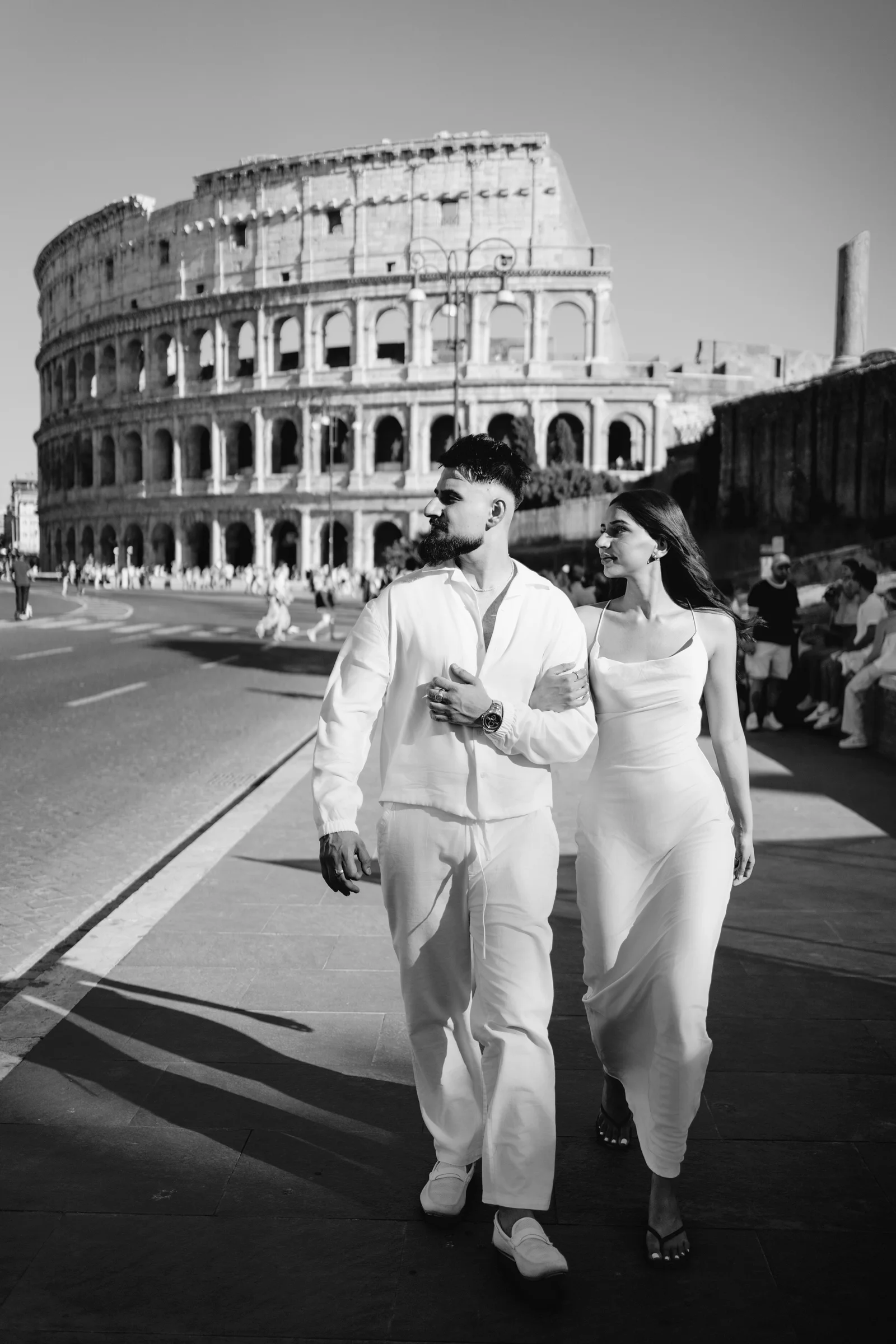 An engagement photographer in Rome captures a couple walking arm-in-arm by the Colosseum in this B&W photo.