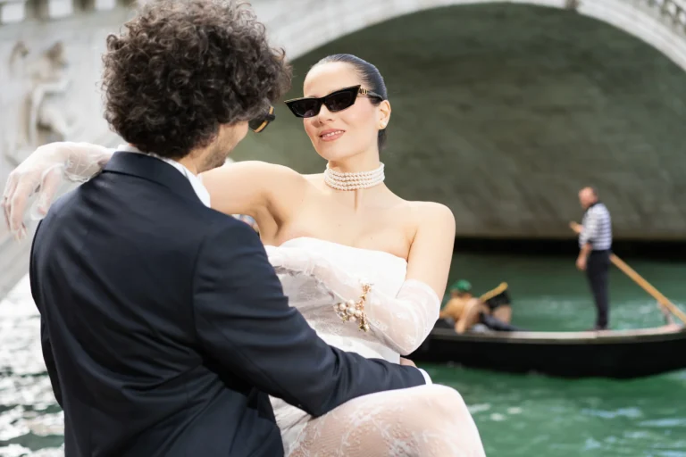 A stylish couple in wedding attire and sunglasses pose for their wedding photographer in Venice.