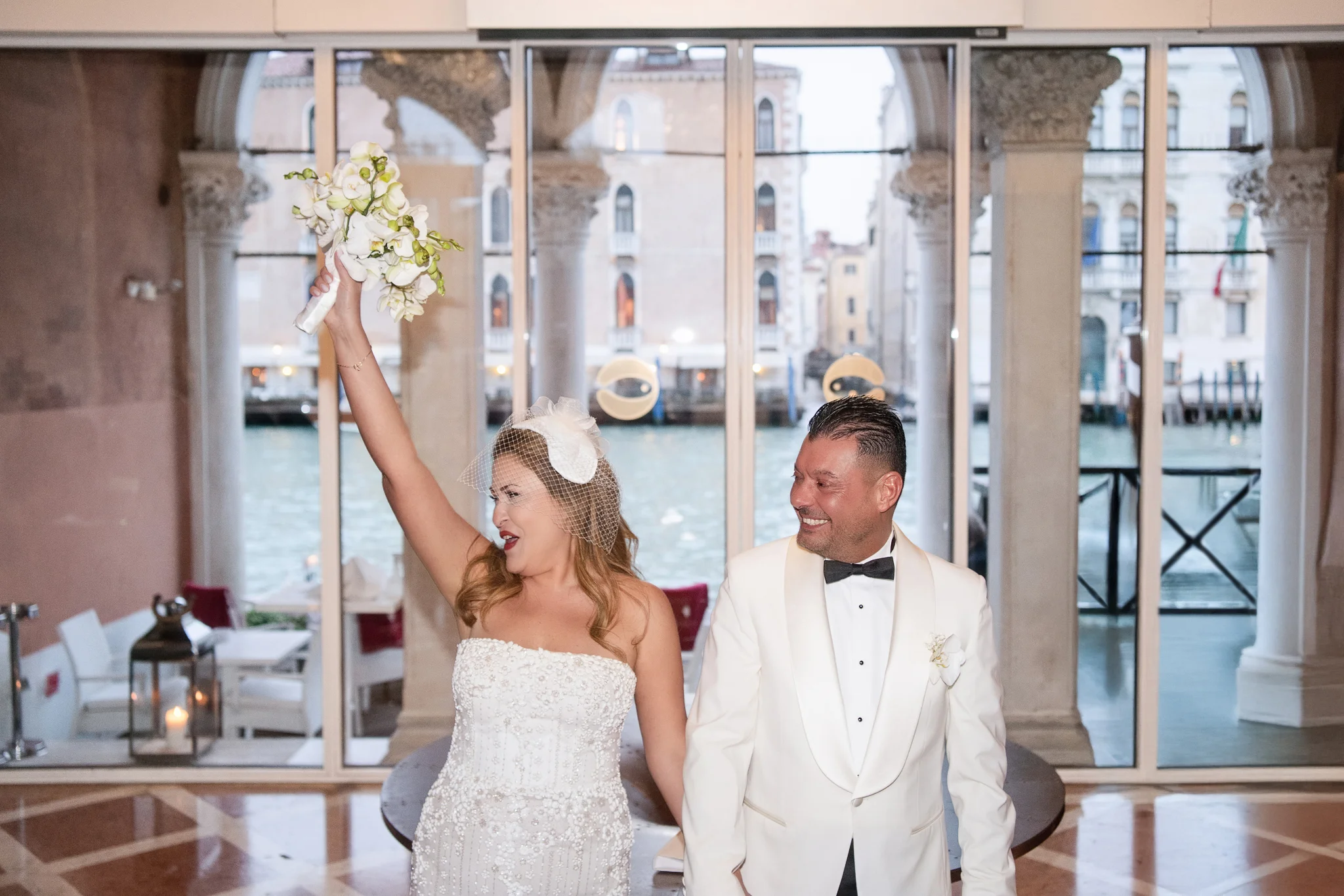 A bride cheers with her bouquet next to her groom, work by a wedding photographer in Venice.