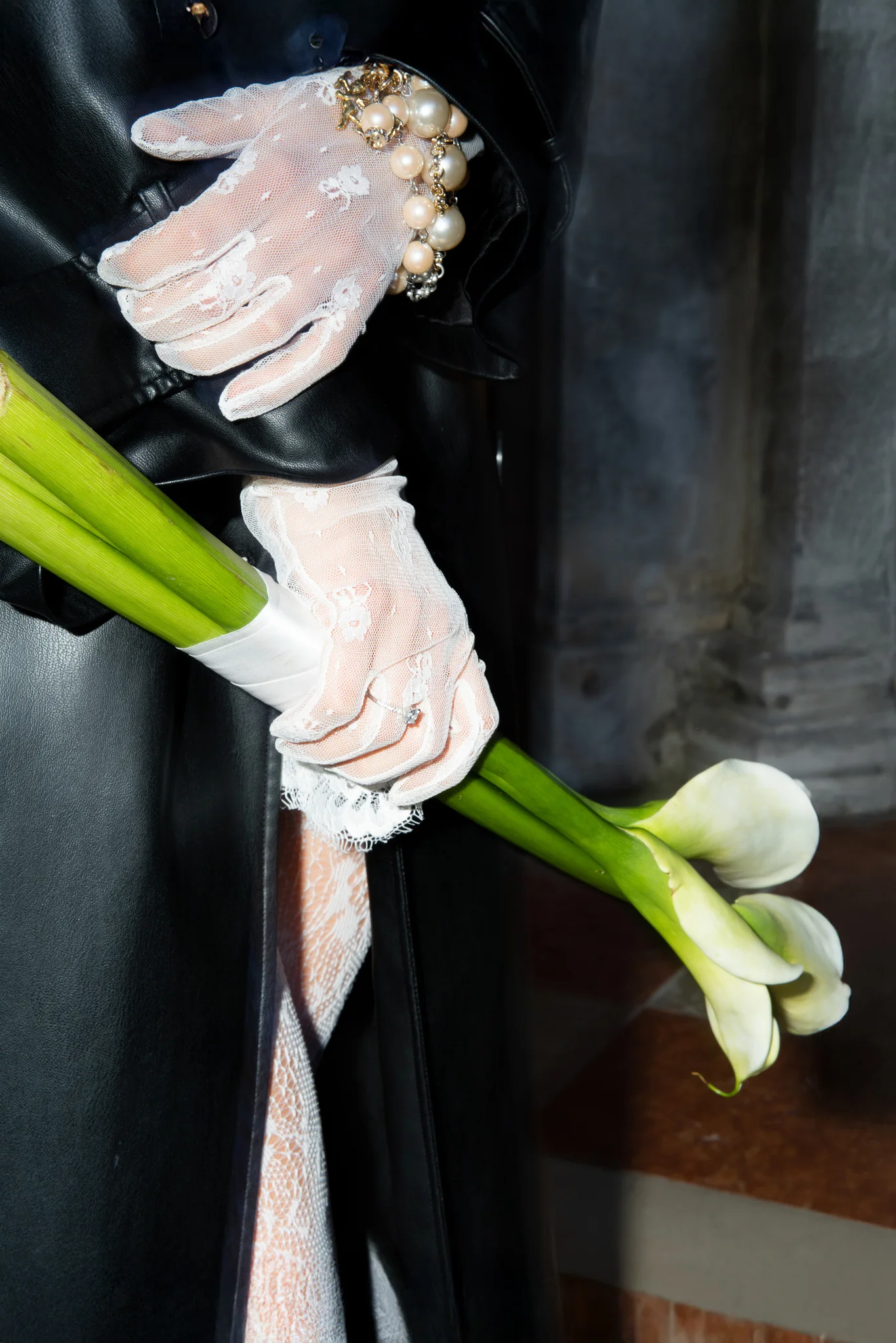 A close-up of a bride's hands in white lace gloves holding a white calla lily bouquet.