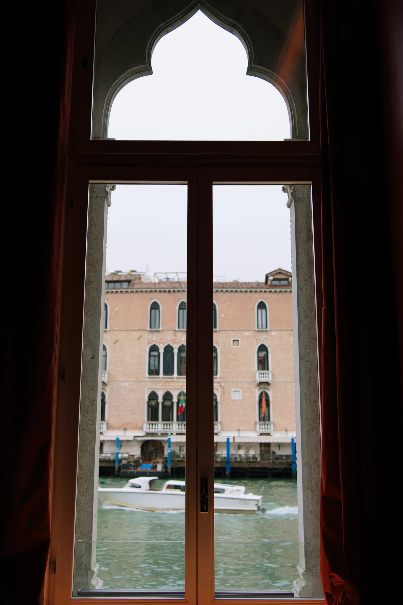 View through an arched window overlooking a canal in Venice with a boat passing by.