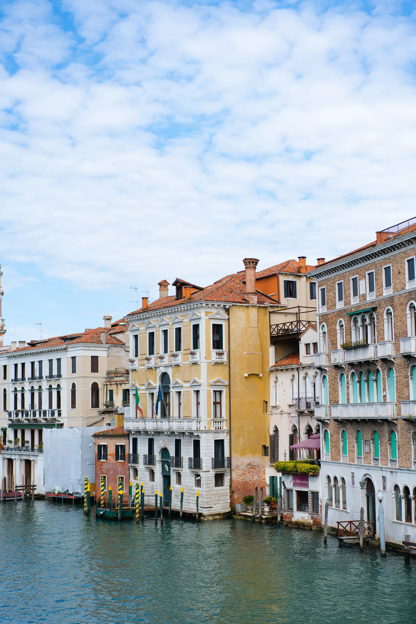 Historic, colorful buildings line the Grand Canal in Venice under a blue, cloudy sky.