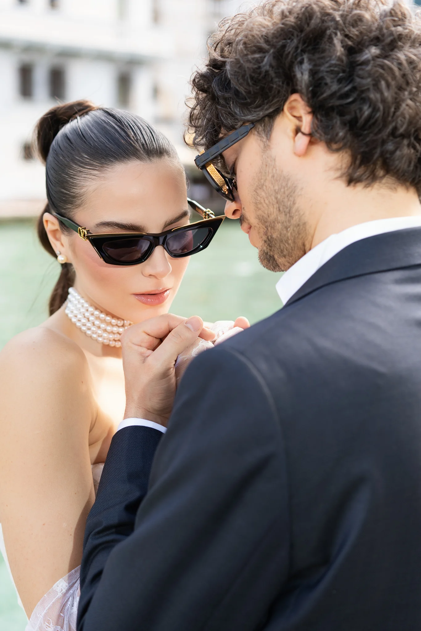 An intimate close-up of a bride and groom, both wearing sunglasses, holding hands in Venice.