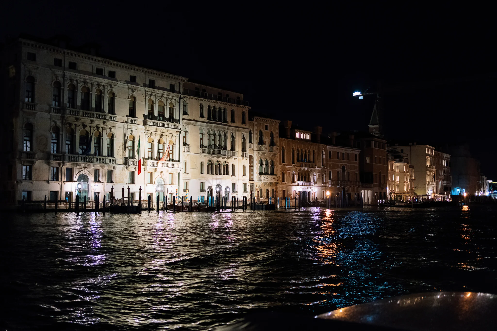 A nighttime view of beautifully illuminated historic buildings along a Venice canal.